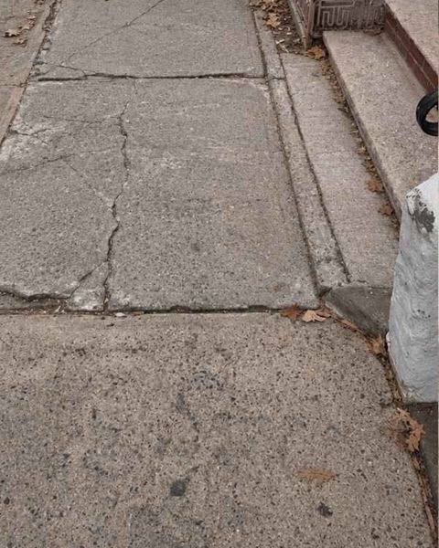 Full-depth cracks and uneven joints in the sidewalk outside 231 Calyer St in Brooklyn before repair