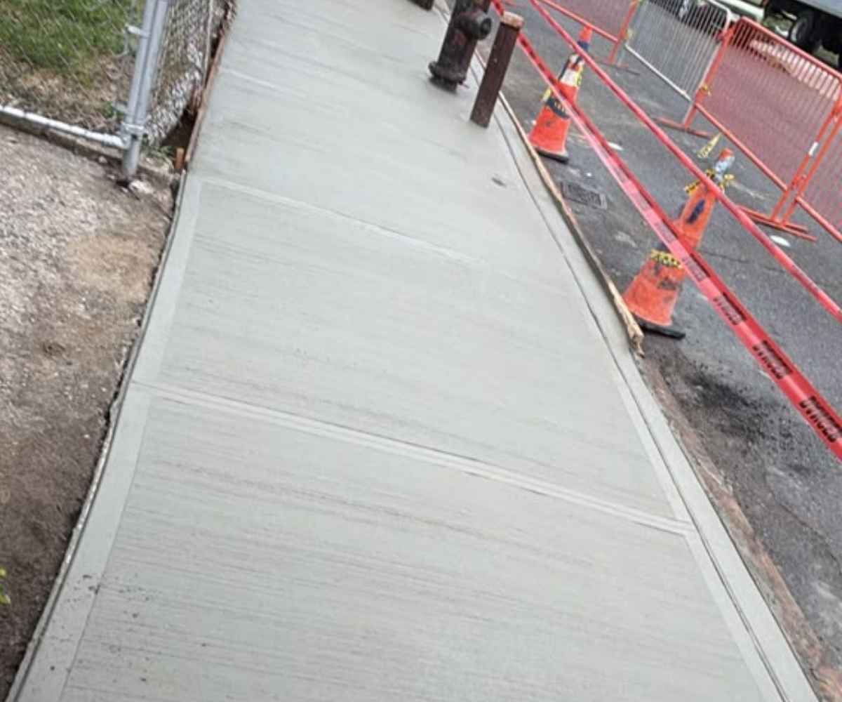 Completed sidewalk and curb reconstruction in freshly poured concrete along the Brunswick Ave frontage